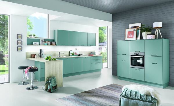 Moderne Küche mit mintgrünen Fronten, Einbaugeräten und heller Arbeitsplatte im Tageslicht.