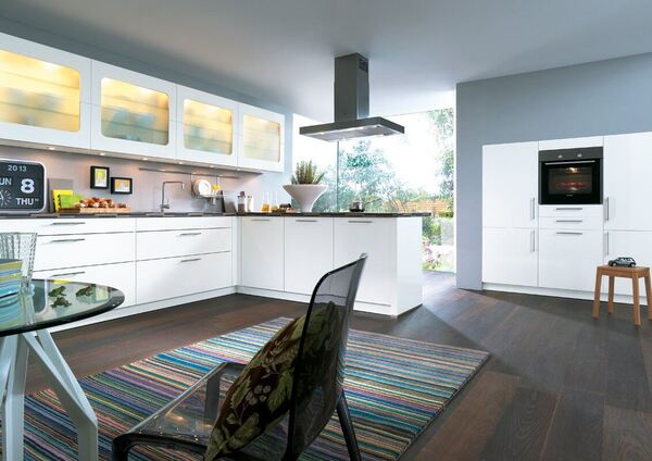 Moderne, helle Einbauküche mit weißen Hochglanzfronten und großem Fenster im Hintergrund.