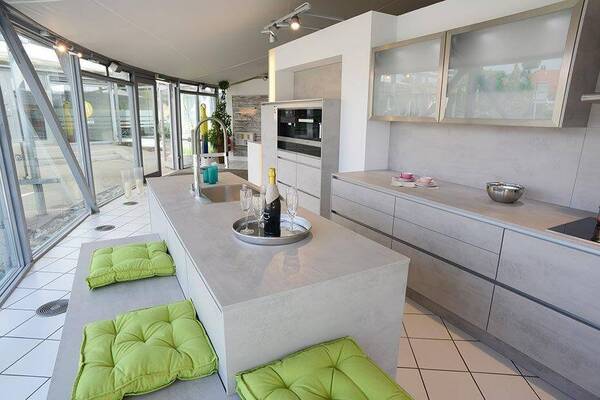 Moderne offene Küche mit heller Kochinsel, grünen Sitzkissen und großen Fenstern.