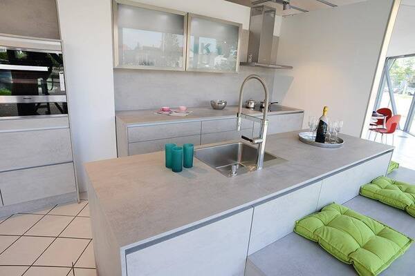 Moderne, helle Einbauküche mit Kochinsel, Edelstahlspüle und grünen Sitzkissen.