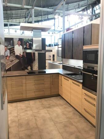 Moderne Einbauküche mit Holzfronten, Elektrogeräten und Kochinsel in Ausstellungsraum.