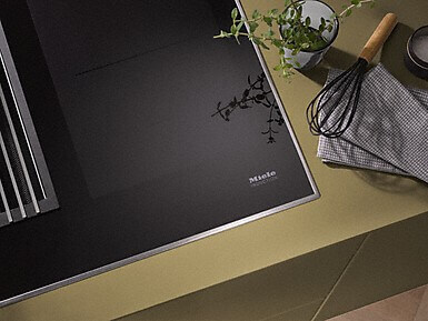 Modernes Miele Induktionskochfeld mit Küchenutensilien und frischer Kräuterpflanze.